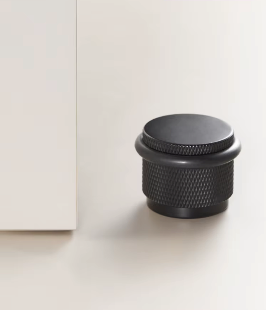 Knurled floor door stop in matte black with a protective rubber ring beside a white door