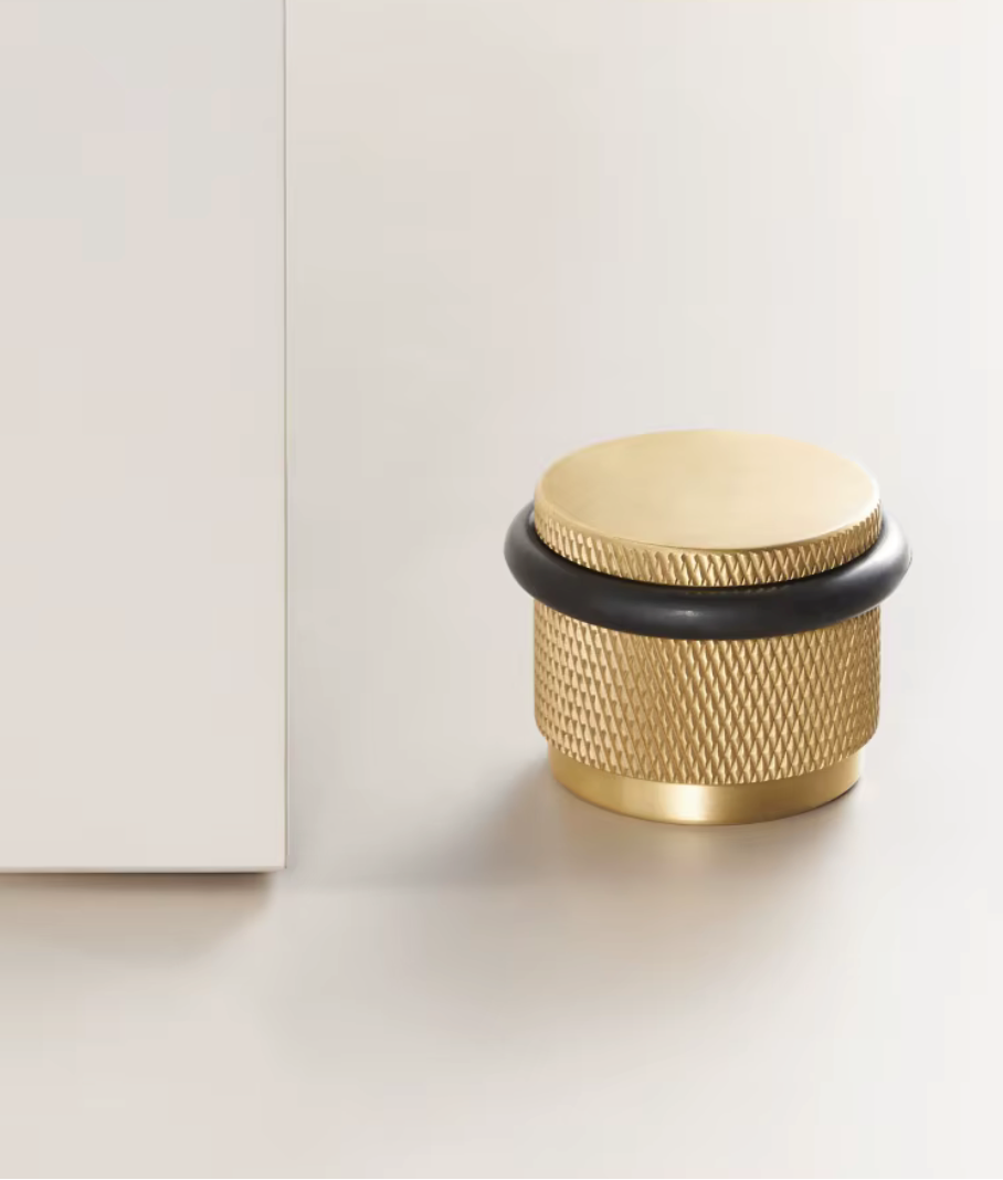 Solid brass knurled floor door stop in brass with a black rubber ring beside a white door