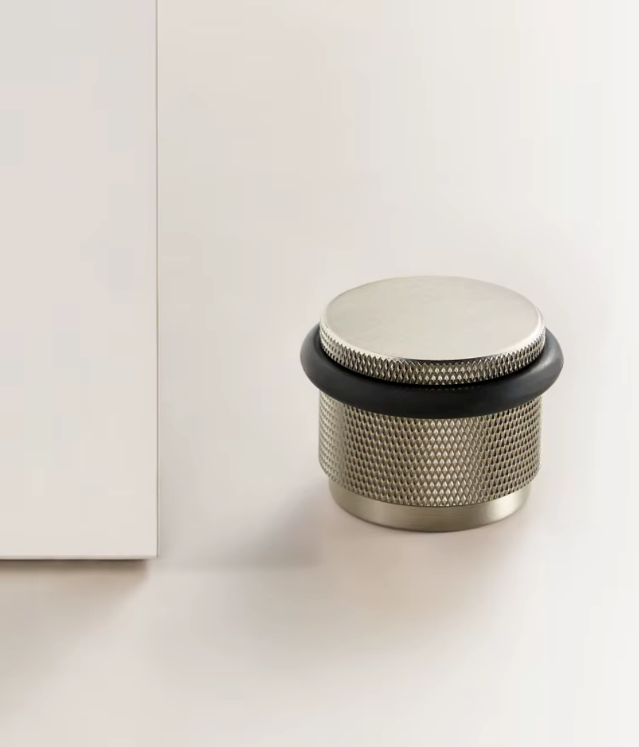  Knurled floor door stop in satin nickel with a black rubber ring beside a white door
