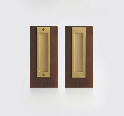Two matching rectangular pocket door pulls with a brushed brass center plate and a dark brown wood surround, shown side by side on a clean white background.